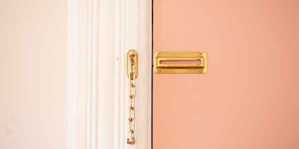 An open door chain lock on a pink door.