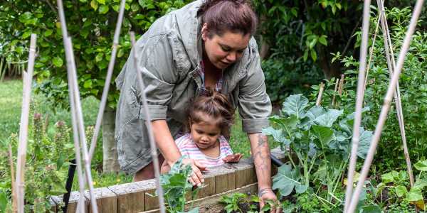 woman tending to a vegetable garden with her child