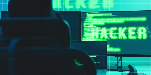 A cheesy image of a hacker sitting at a desk with green test on a computer screen to represent cyber security.