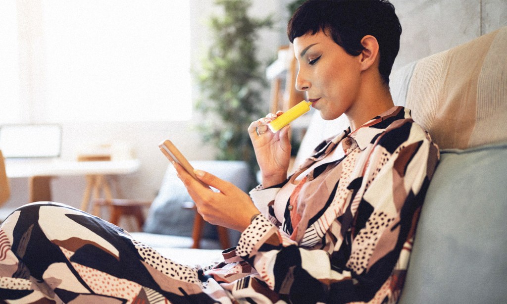 Vape laws in Qld could radically change after the state launched a parliamentary inquiry. Image shows a woman sitting on a sofa using a vape.