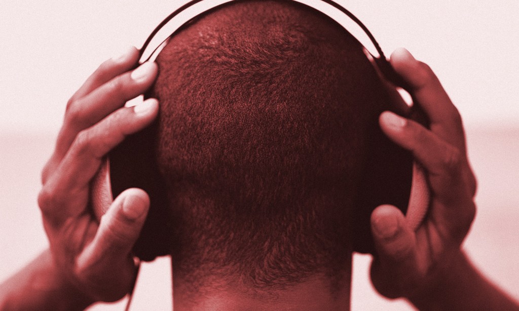 Image shows the back of a man's head wearing headphones as he listens to music to illustrate songs getting stuck in people's heads or the phenomenon known as earworms.