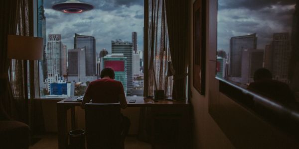 An image showing a ufo floating above a city while a man works.