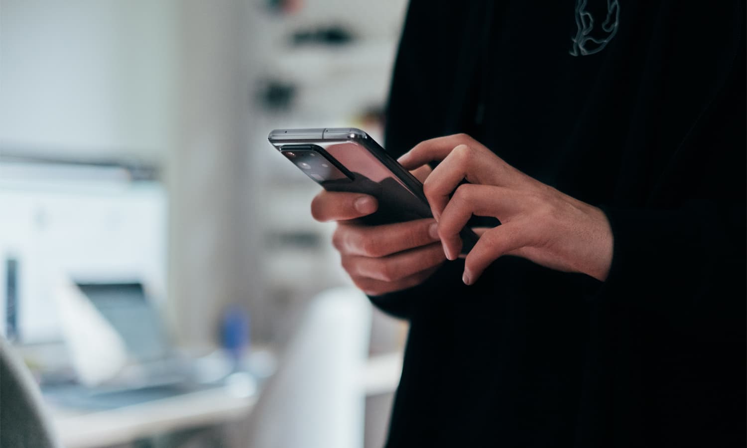 Close-up of someone in a black jumper using a phone.